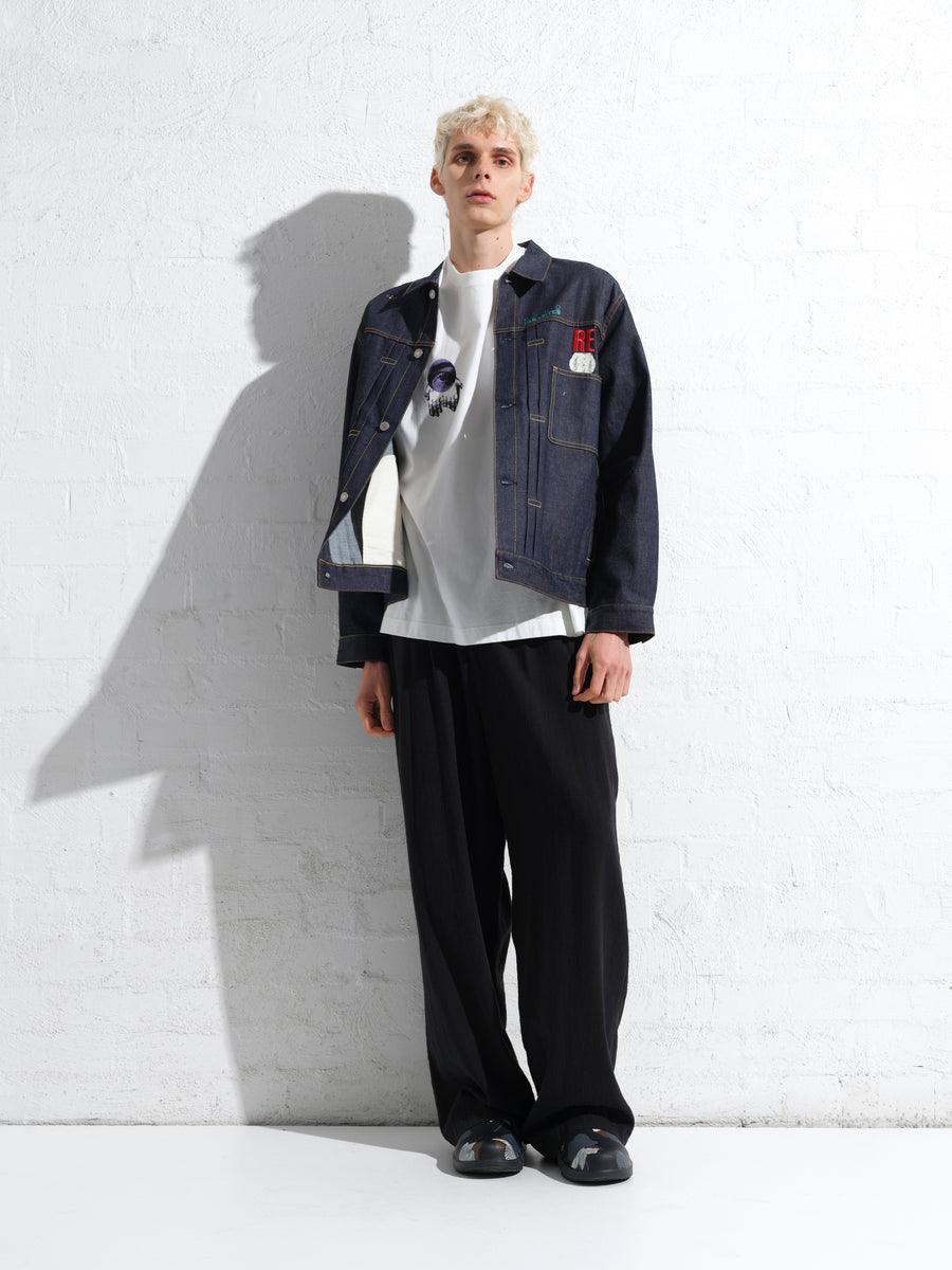 Undercover look from the MARAIS campaign: a raw denim jacket and black trousers against a white wall